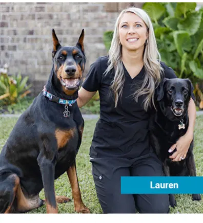 Lauren smiling on a lawn with two dogs